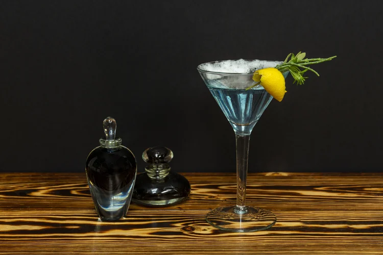 A blue cocktail with a lemon twist beside dark apothecary bottles