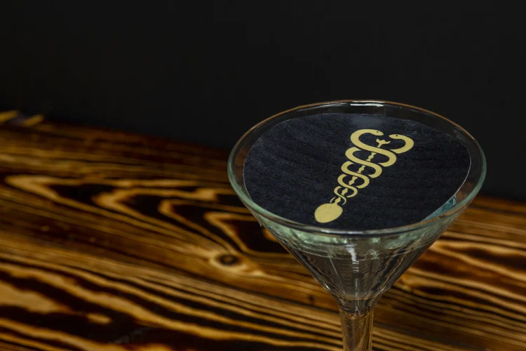 A cocktail dusted with the gold Mama Xanadu caduceus on its surface