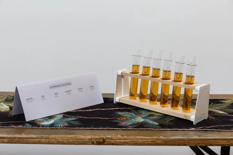 A Goddess Elixirs menu card beside a rack of amber elixir test tubes